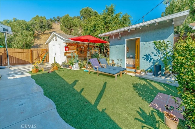 view of yard with a storage shed, fence, a patio, and an outbuilding