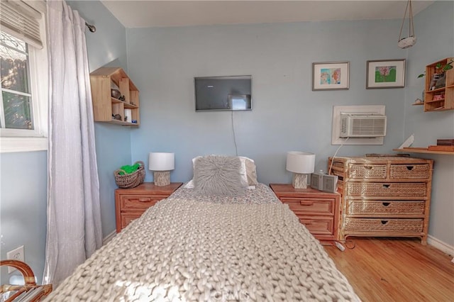 bedroom with a wall unit AC, baseboards, and wood finished floors