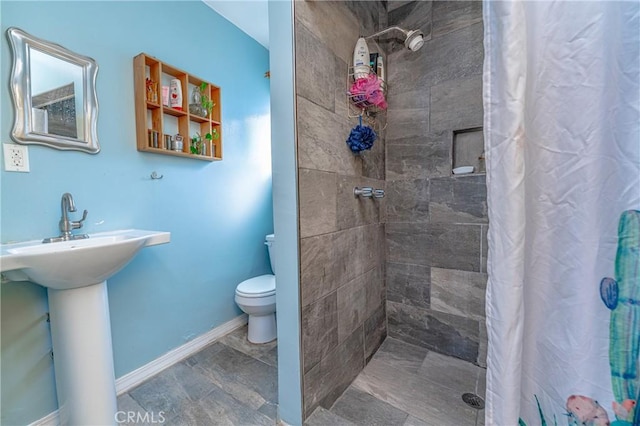 bathroom featuring a sink, a tile shower, toilet, and baseboards