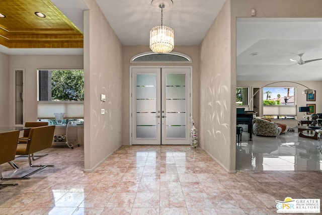 foyer entrance with ceiling fan with notable chandelier, french doors, and a raised ceiling