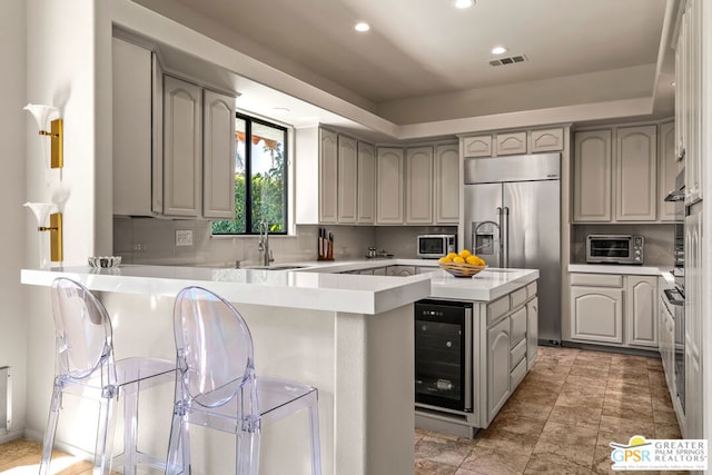 kitchen with sink, gray cabinetry, stainless steel appliances, wine cooler, and kitchen peninsula