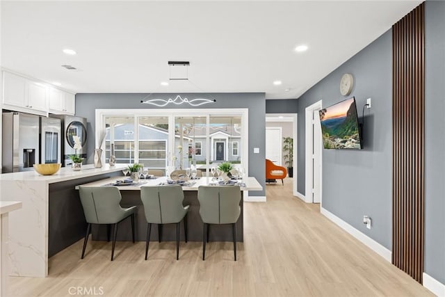 kitchen with stainless steel refrigerator with ice dispenser, kitchen peninsula, light wood-type flooring, a kitchen breakfast bar, and white cabinets