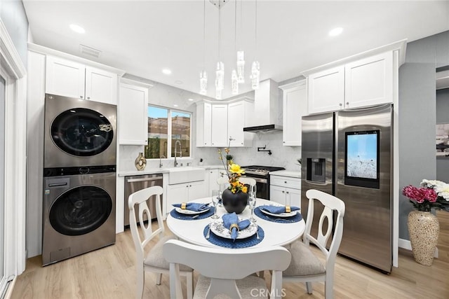 kitchen featuring sink, stacked washer and dryer, appliances with stainless steel finishes, white cabinets, and wall chimney exhaust hood