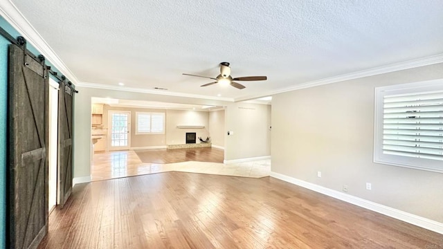 unfurnished living room with a barn door, ceiling fan, light wood-type flooring, a textured ceiling, and ornamental molding