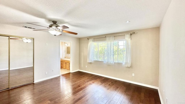 unfurnished bedroom featuring ceiling fan, ensuite bathroom, dark hardwood / wood-style floors, a textured ceiling, and a closet