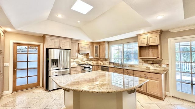 kitchen with light brown cabinets, appliances with stainless steel finishes, a center island, and tasteful backsplash