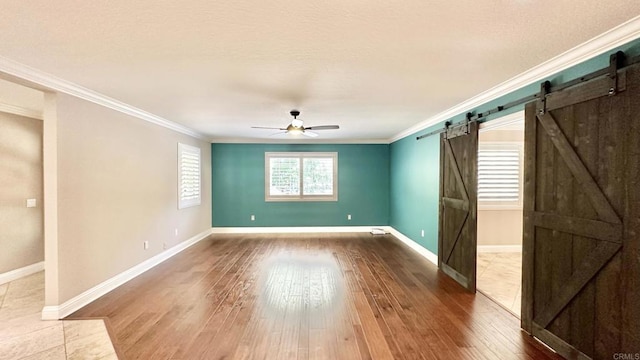 unfurnished room featuring ceiling fan, hardwood / wood-style floors, ornamental molding, and a barn door