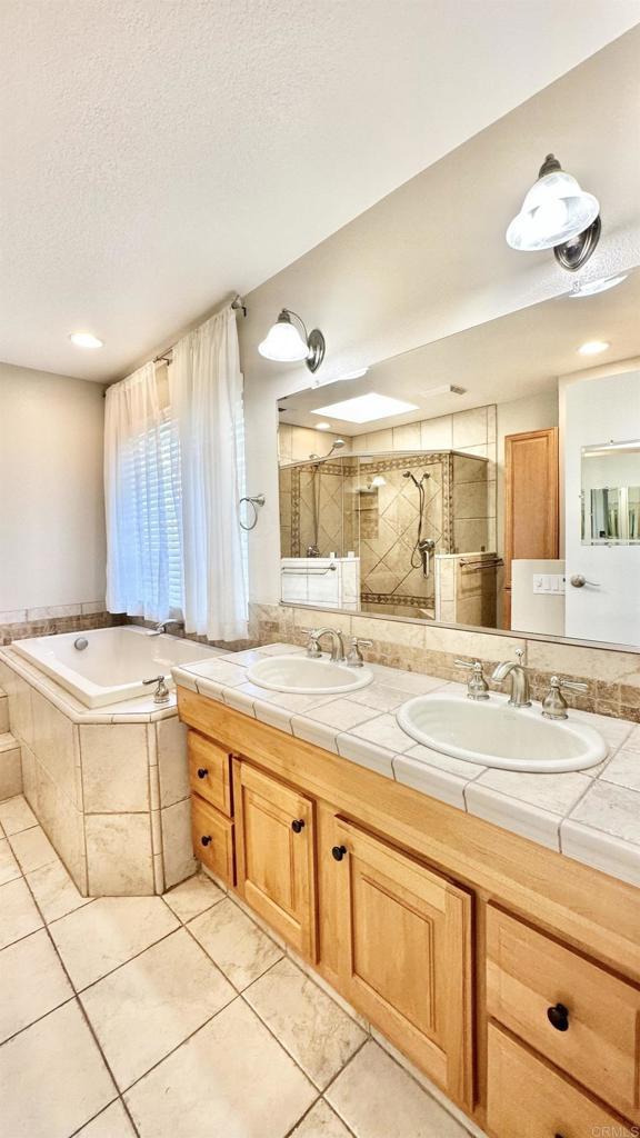 bathroom with a textured ceiling, plus walk in shower, vanity, and tile patterned flooring