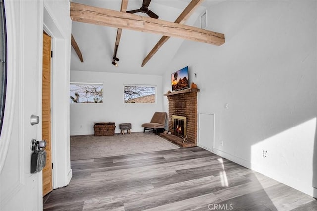 living room with ceiling fan, a fireplace, wood-type flooring, beamed ceiling, and high vaulted ceiling