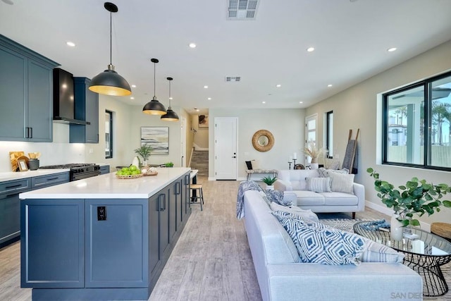 kitchen featuring light wood-type flooring, a kitchen island, hanging light fixtures, and wall chimney range hood