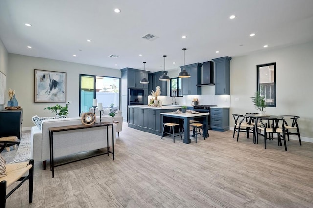 kitchen with wall chimney exhaust hood, pendant lighting, blue cabinets, and light hardwood / wood-style flooring