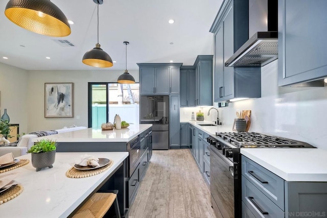 kitchen featuring appliances with stainless steel finishes, wall chimney range hood, light hardwood / wood-style floors, sink, and hanging light fixtures