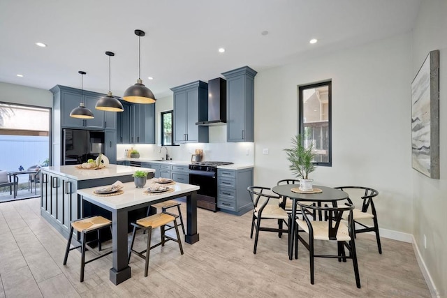 kitchen with black appliances, blue cabinetry, pendant lighting, wall chimney exhaust hood, and sink