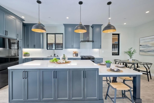 kitchen with hanging light fixtures, stove, wall chimney exhaust hood, and sink