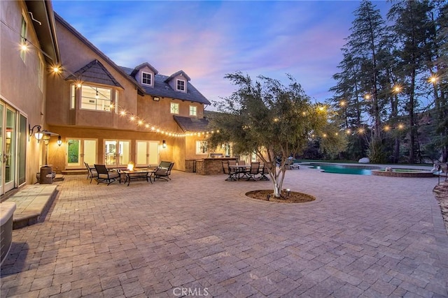 patio terrace at dusk featuring a pool with hot tub, a fire pit, and area for grilling