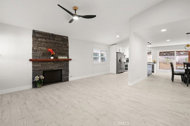 living room with ceiling fan, lofted ceiling, light hardwood / wood-style floors, and a stone fireplace