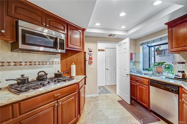 kitchen with light stone countertops, stainless steel appliances, tasteful backsplash, sink, and a tray ceiling