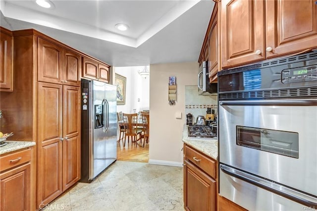 kitchen with tasteful backsplash, light stone counters, stainless steel appliances, and a raised ceiling