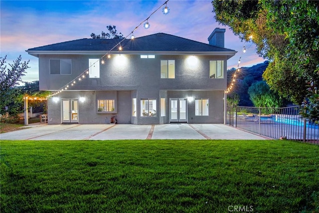 back house at dusk featuring a fenced in pool, french doors, a yard, and a patio