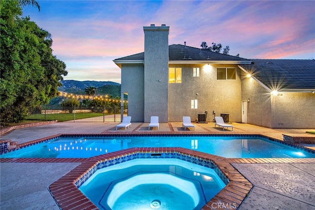 pool at dusk featuring an in ground hot tub, a mountain view, and a patio