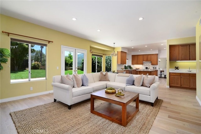 living room with light hardwood / wood-style floors, sink, french doors, and an inviting chandelier