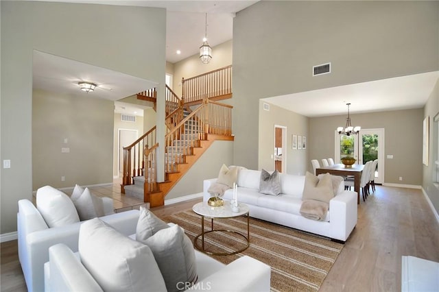 living room with an inviting chandelier, a towering ceiling, and light hardwood / wood-style flooring