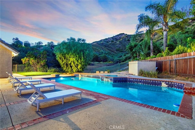 pool at dusk featuring a patio area, a mountain view, and an in ground hot tub