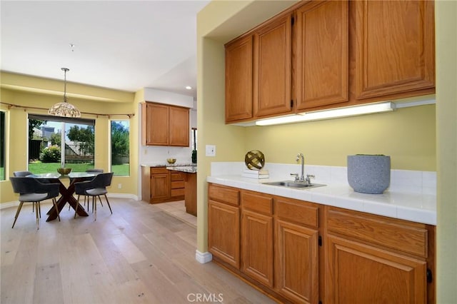 kitchen featuring decorative light fixtures, light hardwood / wood-style floors, tile counters, and sink