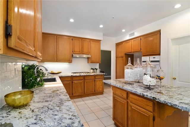 kitchen with white oven, light tile patterned floors, stainless steel gas cooktop, light stone countertops, and sink