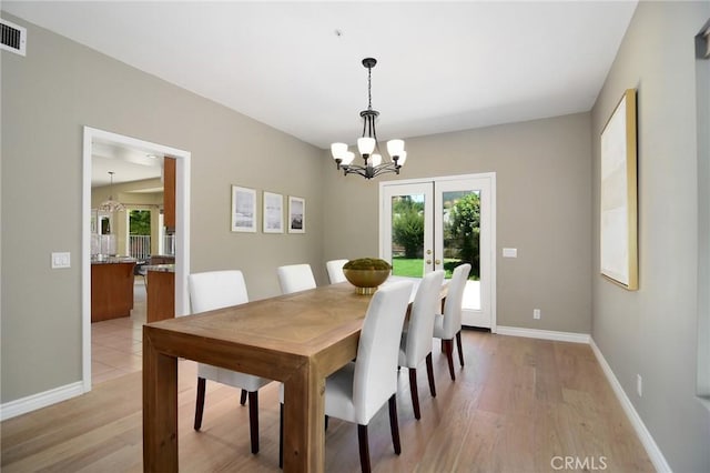 dining room with light wood-type flooring, french doors, and a notable chandelier