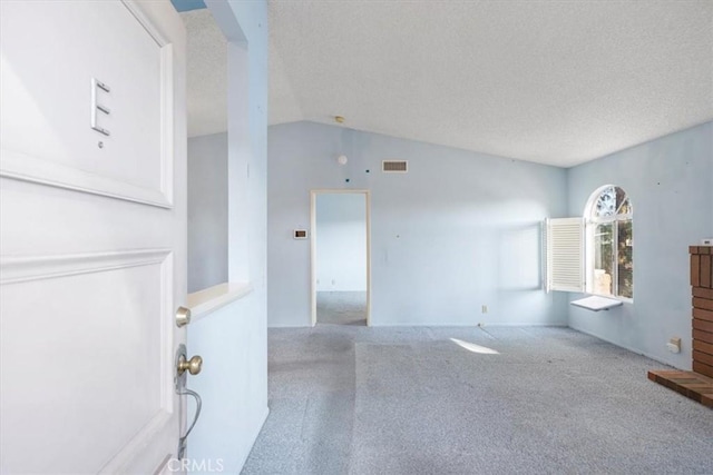 unfurnished living room featuring lofted ceiling, light carpet, and a textured ceiling