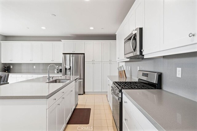 kitchen featuring white cabinets, stainless steel appliances, sink, light tile patterned flooring, and a center island with sink