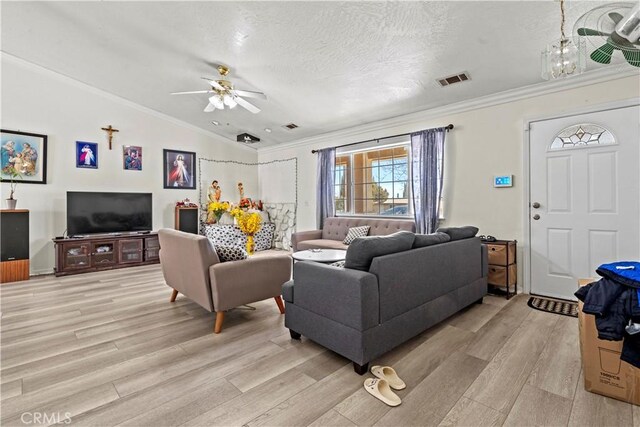 living room with light hardwood / wood-style floors, a textured ceiling, ornamental molding, and vaulted ceiling