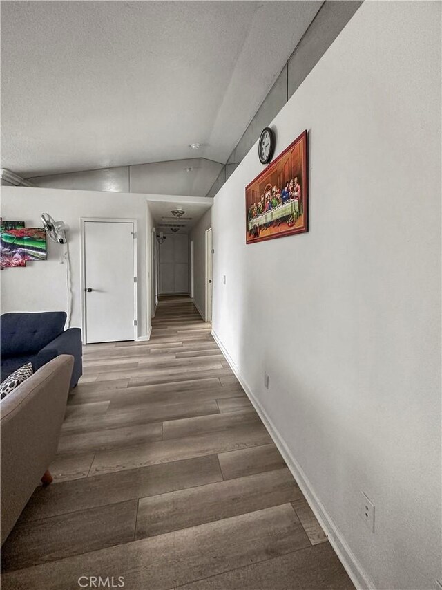 hall with vaulted ceiling, a textured ceiling, and hardwood / wood-style floors