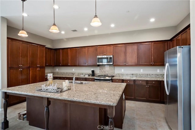 kitchen with sink, hanging light fixtures, stainless steel appliances, and an island with sink