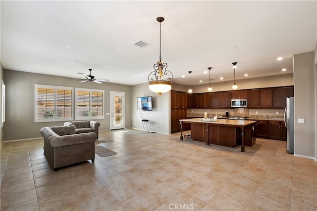 kitchen with appliances with stainless steel finishes, an island with sink, hanging light fixtures, ceiling fan, and a breakfast bar area