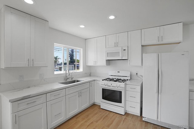 kitchen with light stone countertops, white cabinetry, sink, and white appliances