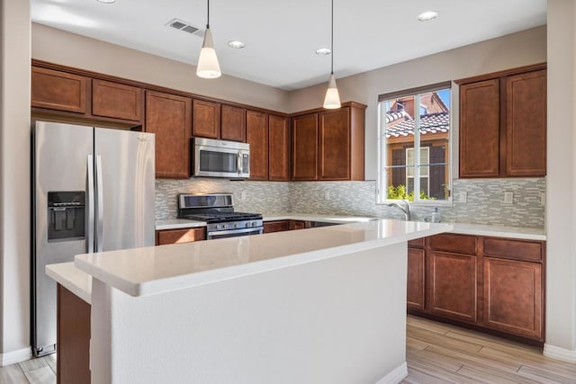 kitchen featuring light hardwood / wood-style flooring, hanging light fixtures, a kitchen island, stainless steel appliances, and backsplash