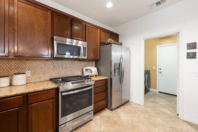 kitchen with light stone countertops, appliances with stainless steel finishes, washer / dryer, and tasteful backsplash