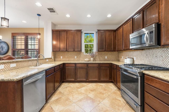 kitchen with stainless steel appliances, sink, light stone counters, and decorative light fixtures