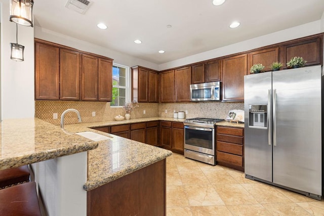 kitchen featuring stainless steel appliances, backsplash, hanging light fixtures, kitchen peninsula, and light stone counters