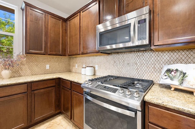 kitchen featuring stainless steel appliances, backsplash, and light stone counters