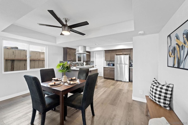 dining room featuring a raised ceiling, ceiling fan, and light hardwood / wood-style flooring