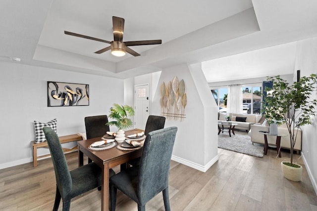 dining space with a raised ceiling, ceiling fan, and light hardwood / wood-style flooring