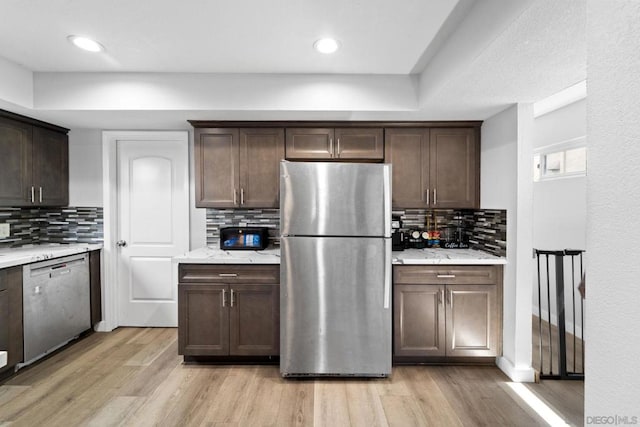 kitchen featuring light stone countertops, stainless steel appliances, decorative backsplash, light wood-type flooring, and dark brown cabinets