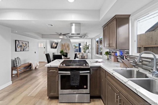 kitchen with kitchen peninsula, island exhaust hood, a tray ceiling, stainless steel stove, and sink