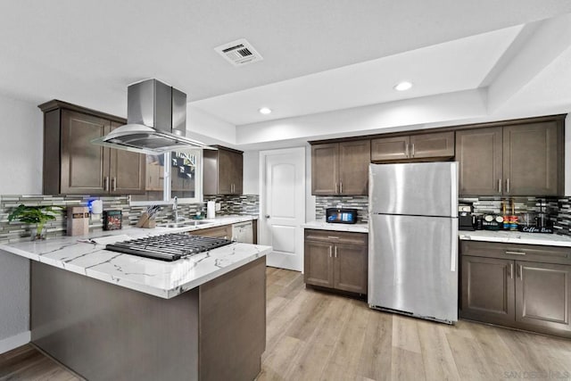 kitchen with island exhaust hood, appliances with stainless steel finishes, kitchen peninsula, and dark brown cabinetry