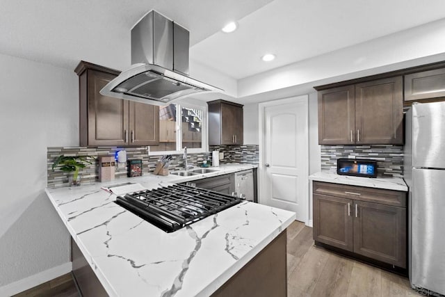 kitchen with island range hood, kitchen peninsula, stainless steel appliances, light stone countertops, and sink