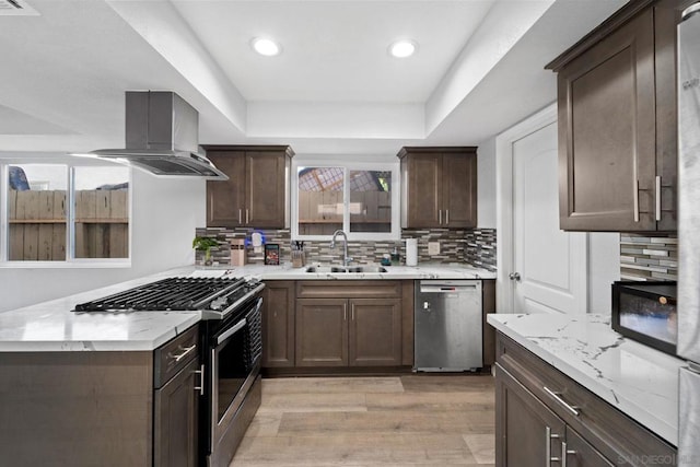 kitchen with appliances with stainless steel finishes, light hardwood / wood-style floors, sink, ventilation hood, and a raised ceiling