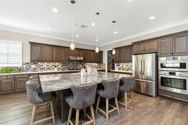 kitchen with light stone countertops, pendant lighting, stainless steel appliances, an island with sink, and a breakfast bar